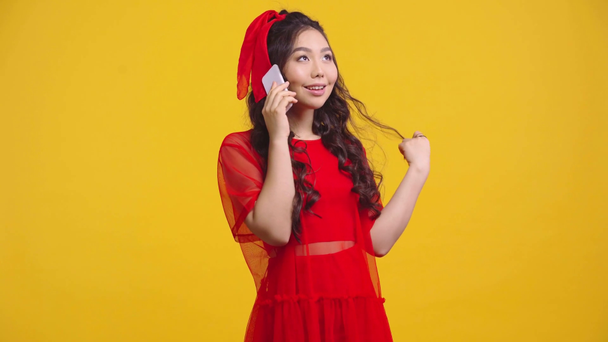 χαρούμενο κορίτσι από την Ασία μιλάει στο smartphone απομονωμένο στο κίτρινο  - Πλάνα, βίντεο