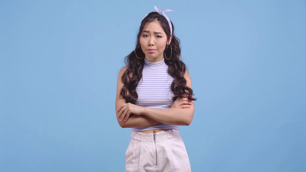 ofendido asiático chica de pie con cruzado brazos aislado en azul
  - Metraje, vídeo