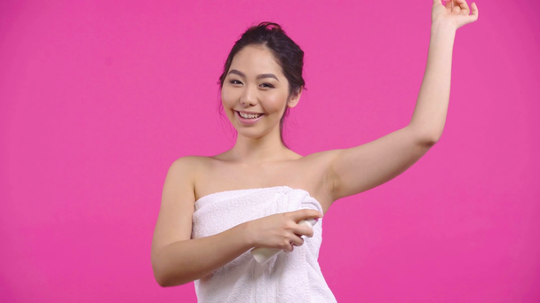 happy asian girl applying deodorant spray isolated on pink  - Footage, Video
