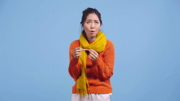 sick asian girl looking at digital thermometer isolated on blue - Séquence, vidéo