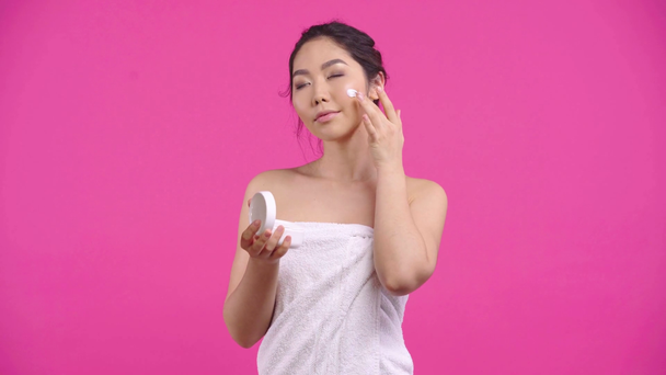 χαρούμενο κορίτσι από την Ασία που απλώνει κρέμα προσώπου απομονωμένη σε ροζ  - Πλάνα, βίντεο