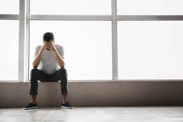 Depressed young man near window - Photo, Image
