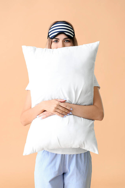 Portrait of young woman in pajamas, with sleep mask and pillow on color background - Photo, Image