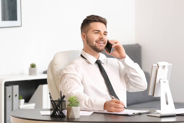 Young businessman talking by mobile phone in office - Foto, imagen