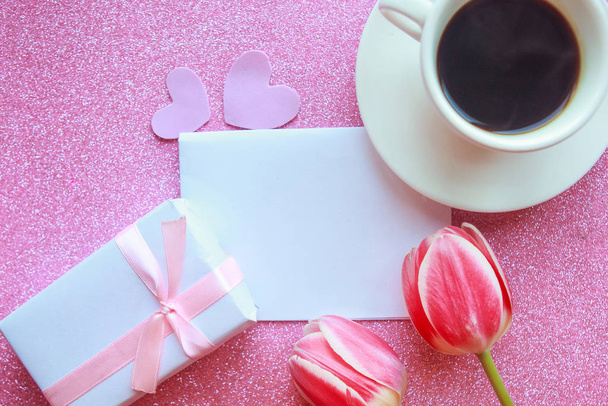 Foto plana con taza de café, caja de regalo y tulipanes rojos sobre fondo rosa. Hermoso Día de la Madre, Día de la Mujer o tarjeta de felicitación de San Valentín. Tarjeta de felicitación maqueta Día de la Madre
 - Foto, Imagen