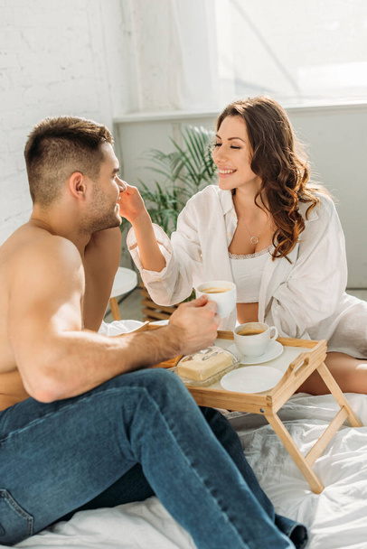 feliz, chica sexy tocando la cara del novio sin camisa cerca de la bandeja de la cama con delicioso desayuno
 - Foto, Imagen