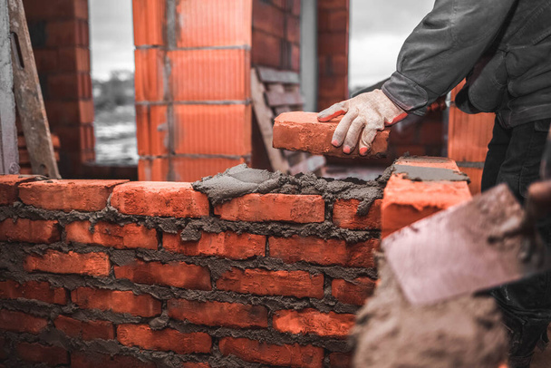 Bricklayer puts bricks to make a wall - Foto, afbeelding