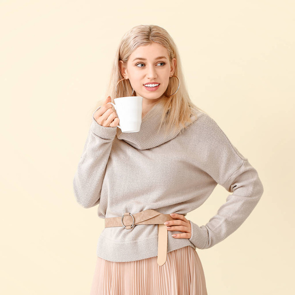 Beautiful young woman in warm sweater drinking tea on color background - Фото, изображение