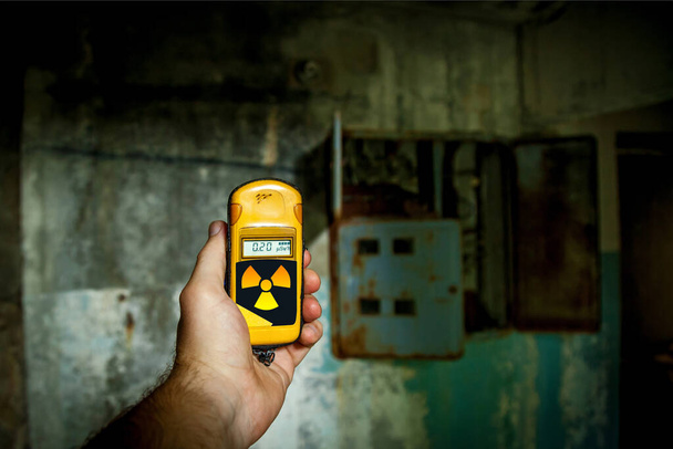 A person tries to check a radiation level with a personal dosimeter near the abandoned building. - Zdjęcie, obraz