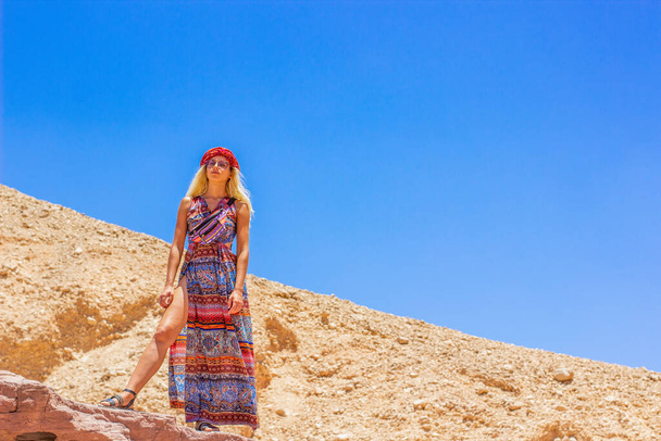 bílá evropská žena klidný portrét v hidžábu a barevné dlouhé šaty v dominantní póze při pohledu na kameru shora pobyt na útesu v pouštní kaňonu skalnaté prostředí, módní plakát, kopírovací prostor - Fotografie, Obrázek