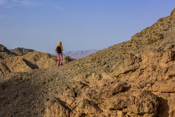 Sırt çantalı kızın seyahat ve yürüyüş fotoğrafçılığı çıplak kaya zemininde kamera karşısında kal ve çölde bir yerlere bak kuru ve vahşi doğa manzarası alanı kopyala - Fotoğraf, Görsel