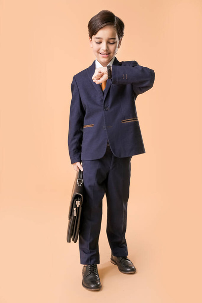 Маленький бизнесмен смотрит на свои наручные часы на цветном фоне
 - Фото, изображение