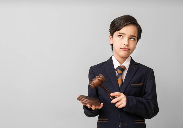 Bedachtzame kleine advocaat met rechter hamer op grijze achtergrond - Foto, afbeelding