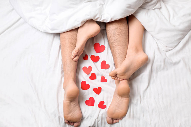 Young couple with red hearts lying in bed, top view - Foto, Imagem