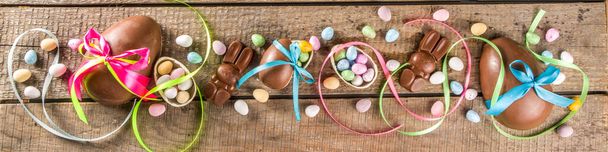 Osterkarten-Hintergrund. Schokolade Ostereier und Hasen mit Farbband und Schleifen auf Holzgrund - Foto, Bild