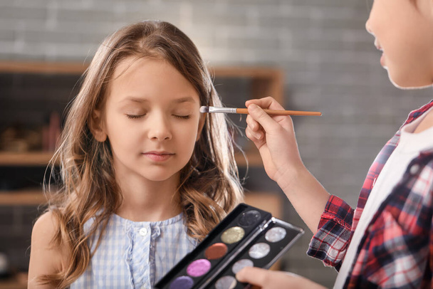 Cute little girl applying makeup on her friend's face at home - Foto, Imagen