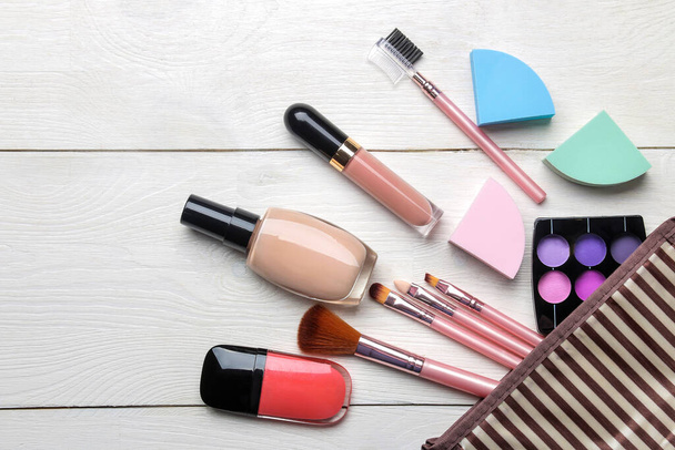 makeup kit. Women's cosmetics in a cosmetic bag and makeup brushes on a white wooden background. top view - Photo, Image