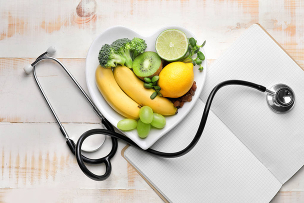 Placa com produtos saudáveis, estetoscópio e caderno na mesa
 - Foto, Imagem