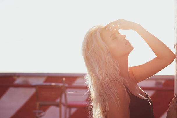 Tyylikäs blondi nainen pukeutuu tyylikäs musta mekko poseeraa katolla aurinkoisena iltana. Tekstitila
 - Valokuva, kuva