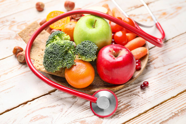 Plate with healthy products and stethoscope on white wooden background - Valokuva, kuva