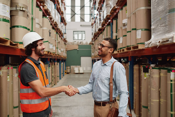 happy young business man in formal clothing making a deal with warehouse manager - two partners shaking hands on a new deal - Photo, Image