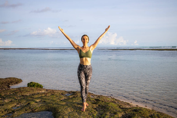 Podróże. Podekscytowana młoda kobieta podnosząca ramiona na plaży przed oceanem. Wolność i energia. Widok na ocean. Odbiór. Plaża Melasti, Bali - Zdjęcie, obraz