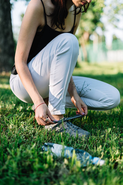 Girl athlete tying shoelaces on sneakers in a summer park. Nearby is a bottle of water - Fotoğraf, Görsel