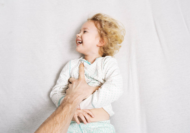 Family time: a little girl lies on the bed and laughs cheerfully because of the tickling of her father. - Foto, immagini
