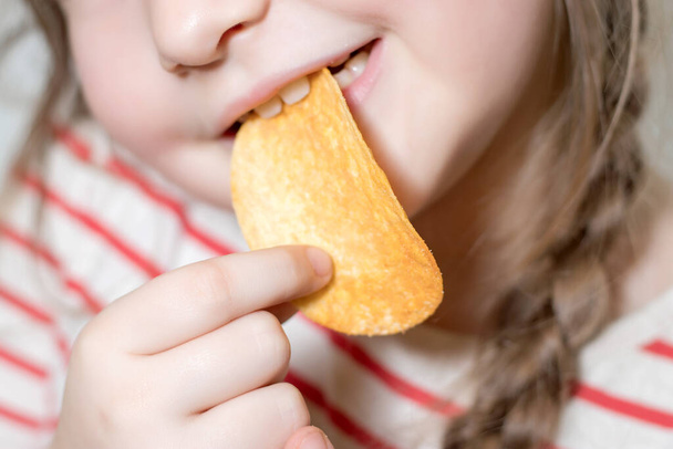 klein meisje eten een aardappel chips. - Foto, afbeelding