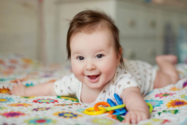 Cute baby boy lying on the bed and play with his colorful toys - Φωτογραφία, εικόνα
