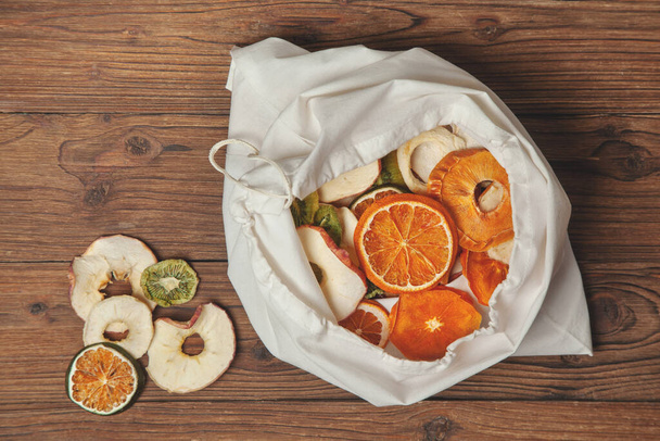 cotton bag with fruit chips on a dark wooden background. view from above - Fotoğraf, Görsel
