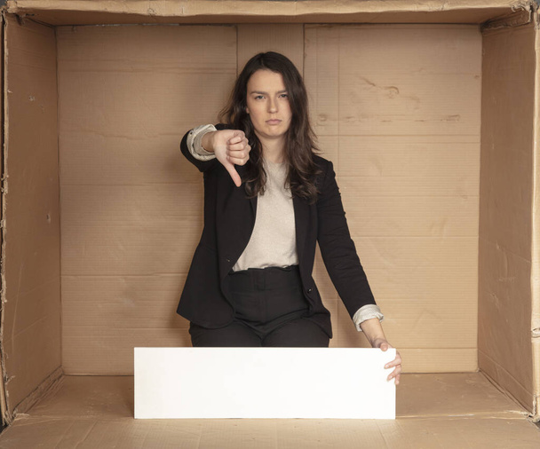 mujer de negocios insatisfecha con espacio para la publicidad sentada en una oficina de cartón vacía
 - Foto, Imagen