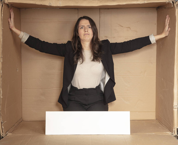 недовольная деловая женщина с местом для рекламы, сидящая в пустом картонном офисе
 - Фото, изображение
