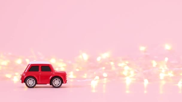 Red toy car for children and a golden blinking garland on a pink background. Holiday concept - Záběry, video