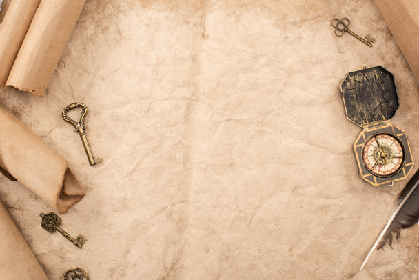 vrchní pohled na archivní klíče a kompas v blízkosti peří na starém papíru - Fotografie, Obrázek