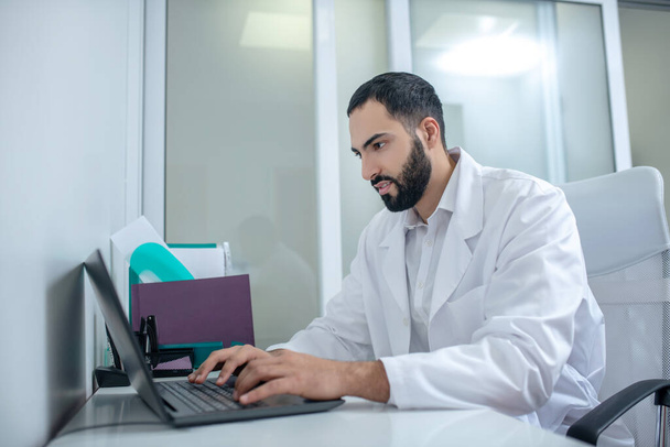 Male doctor in a white robe typing a message - Foto, immagini