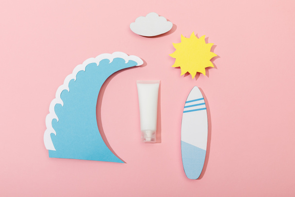 Top view of paper cut sun, cloud, sea wave and surfboard with tube of sunscreen on pink background - Foto, Bild