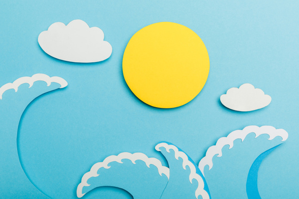 Top view of paper cut sun, clouds and sea waves on blue  - Foto, imagen