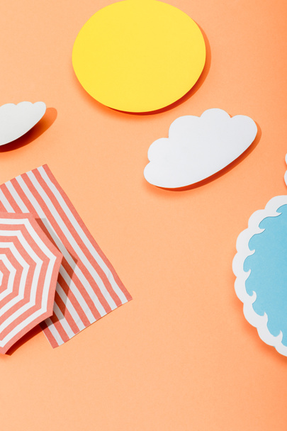 Paper cut sun, clouds, sea wave, beach umbrella and blanket on orange background - Fotografie, Obrázek