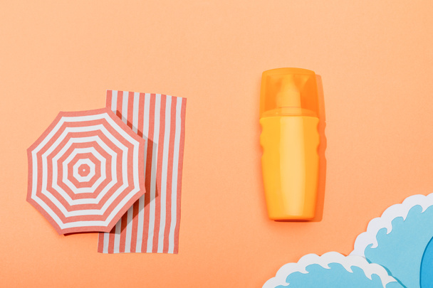 Draufsicht auf Spender Flasche Sonnencreme mit Papier geschnitten Meereswellen auf orangefarbenem Hintergrund - Foto, Bild