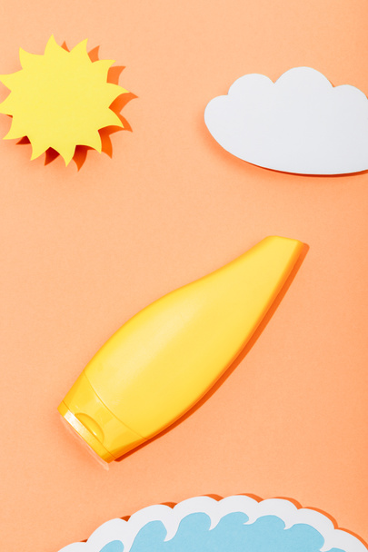 Вид сверху на вырезанное из бумаги солнце, облако и морскую волну с трубкой солнцезащитного крема оранжевого цвета
 - Фото, изображение