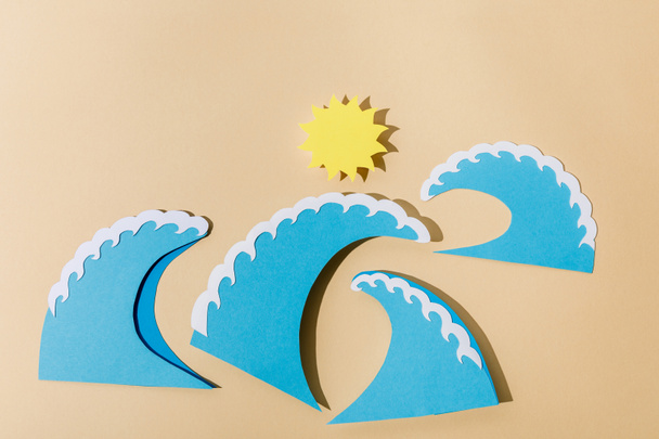 Bovenaanzicht van papier gesneden zon en zee golven op beige  - Foto, afbeelding