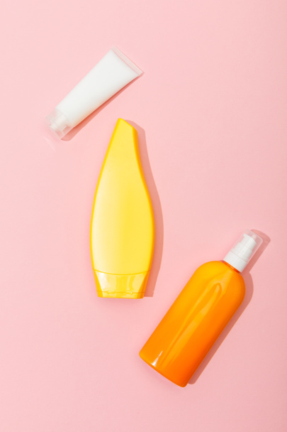 Top view of tubes and dispenser bottle of sunscreen on pink background - Fotoğraf, Görsel