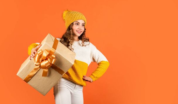 Shopping mall. Birthday celebration idea. Birthday tradition. Fashionable little girl wear knitted hat and sweater. Birthday surprise. Pretty teen makeup face curly hairstyle. Kid hold present box - 写真・画像
