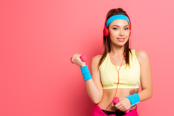 mosolygós sportos nő a fejhallgató képzés súlyzók rózsaszín háttér - Fotó, kép