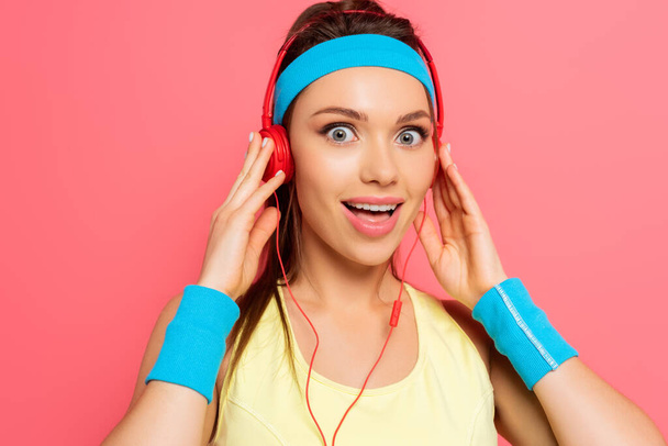 shocked sportswoman touching headphones while looking at camera isolated on pink - Fotoğraf, Görsel