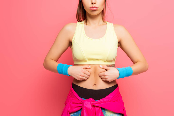 cropped view of displeased sportswoman touching her body on pink background - Foto, afbeelding