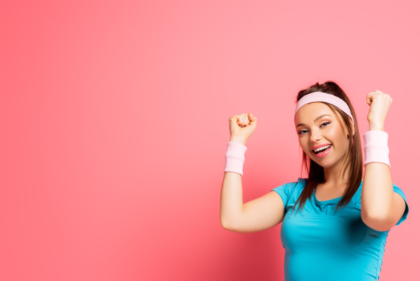 happy sportswoman showing winner gesture while looking at camera on pink background - Fotoğraf, Görsel