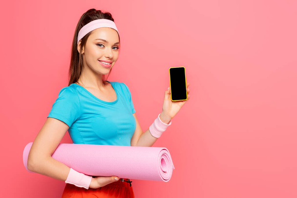 hymyilevä urheilija tilalla kunto matto ja osoittaa älypuhelin tyhjä näyttö eristetty vaaleanpunainen
 - Valokuva, kuva