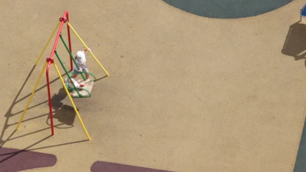 Vista aérea superior del patio de recreo en el día de verano.Una niña irreconocible juega con la muñeca del bebé.Ella lo balancea en un oscilación, entonces otra muchacha vino
 - Metraje, vídeo